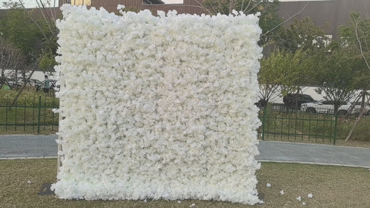 Large white artificial flower wall backdrop set up outdoors, perfect for events like weddings and photoshoots. Is this backdrop weather-resistant for outdoor use? What are the dimensions and how easy is it to assemble? Can the flower density or color be customized for specific themes?