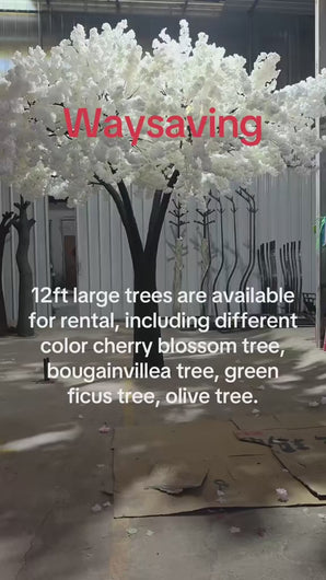 Artificial tree with lush white blossoms and a realistic trunk, displayed in a workshop setting, ready for rental as stunning decor for weddings and events. Are these trees easy to assemble and transport for venue setup?