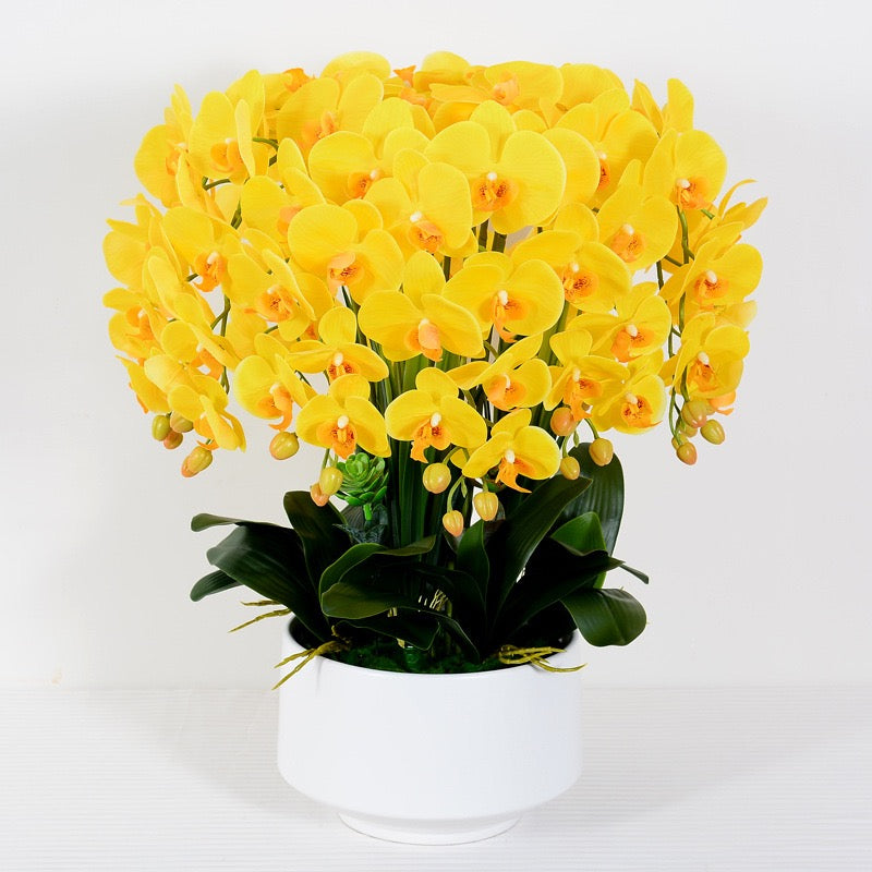 A vibrant arrangement of artificial yellow orchids with realistic petals and buds, displayed in a white ceramic pot. How can I keep artificial flowers looking fresh over time?