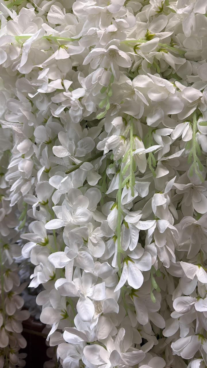 White artificial wisteria floral garland with cascading clusters of small bell-shaped flowers on long green stems.