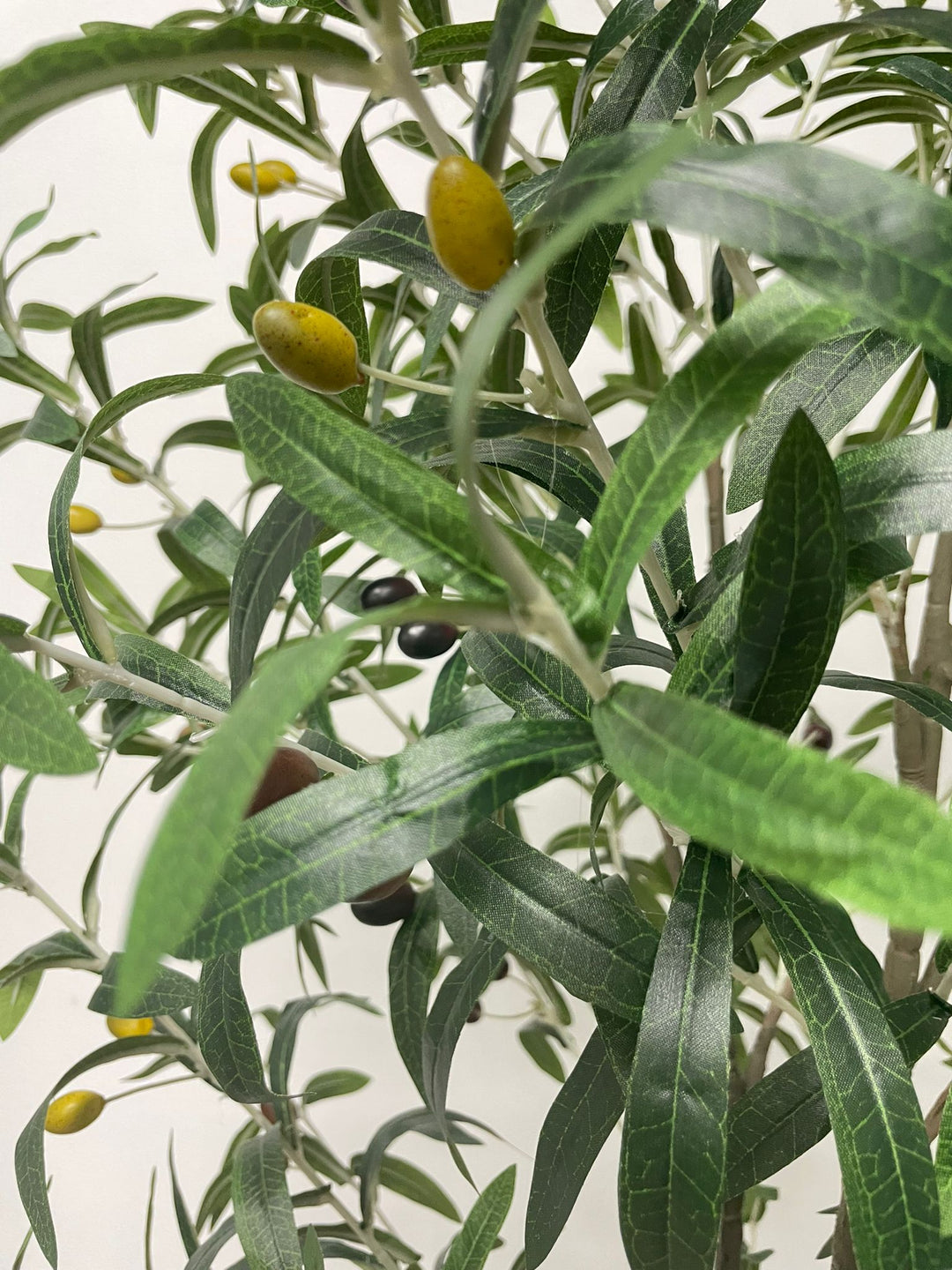 Close-up view of the artificial olive tree's leaves and small dark olives, showing the detailed texture and realistic design of the foliage against a neutral background.