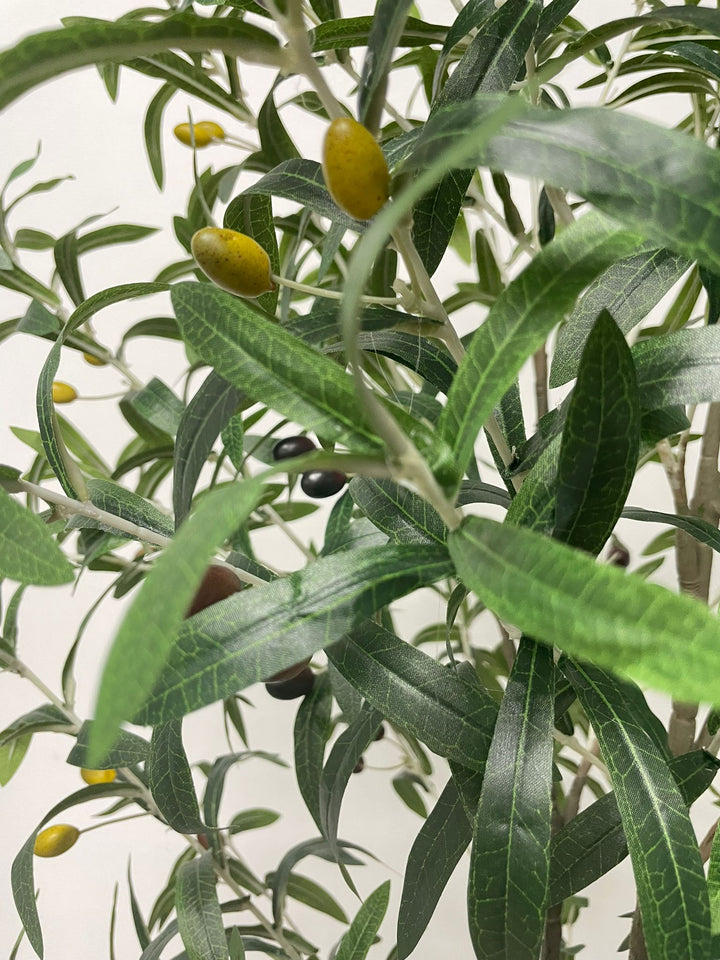 Close-up view of the artificial olive tree's leaves and small dark olives, showing the detailed texture and realistic design of the foliage against a neutral background.
