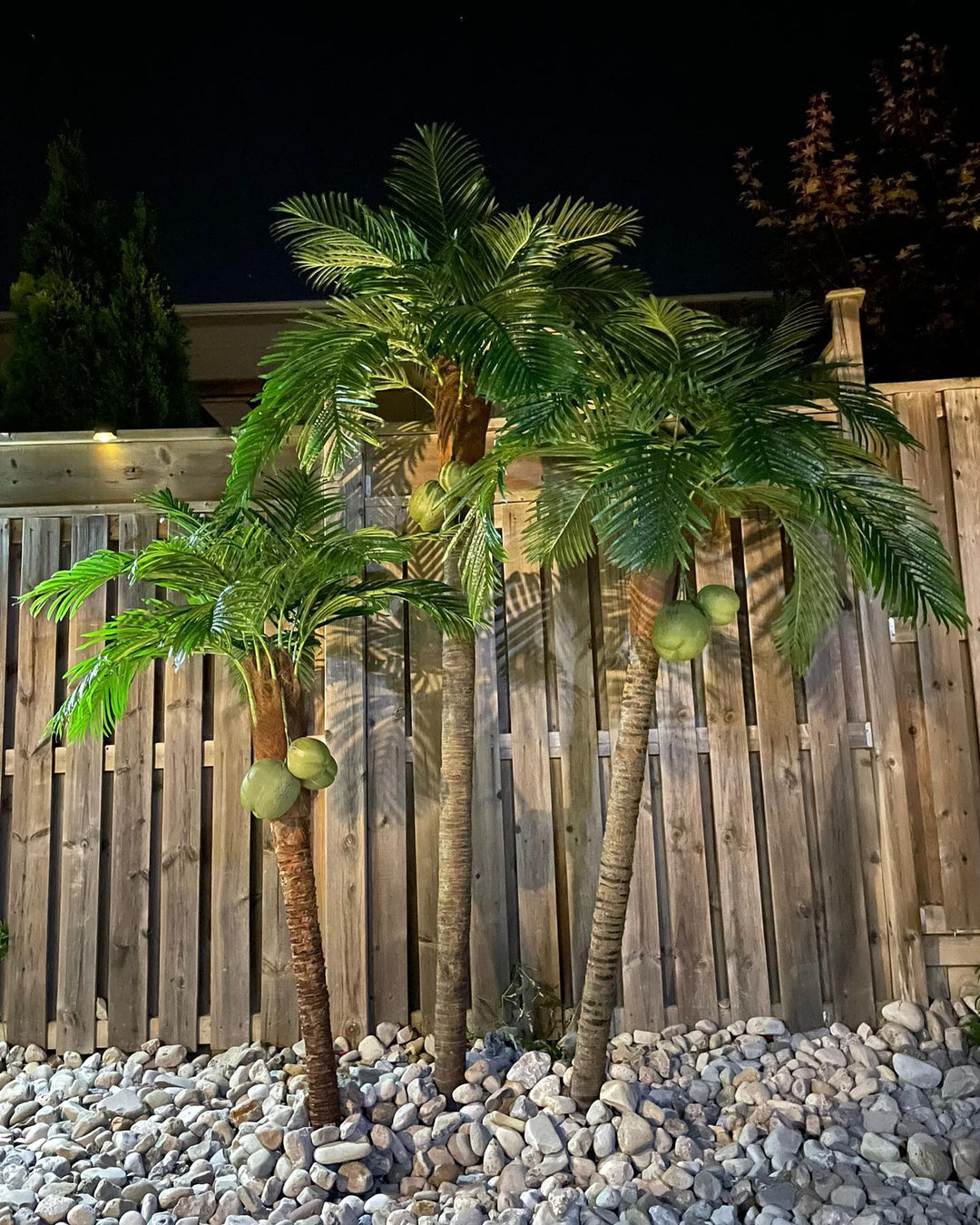 Artificial palm trees with coconuts in an outdoor nighttime setting, illuminated to showcase their realistic appearance, perfect for creating a tropical ambiance in any space.
