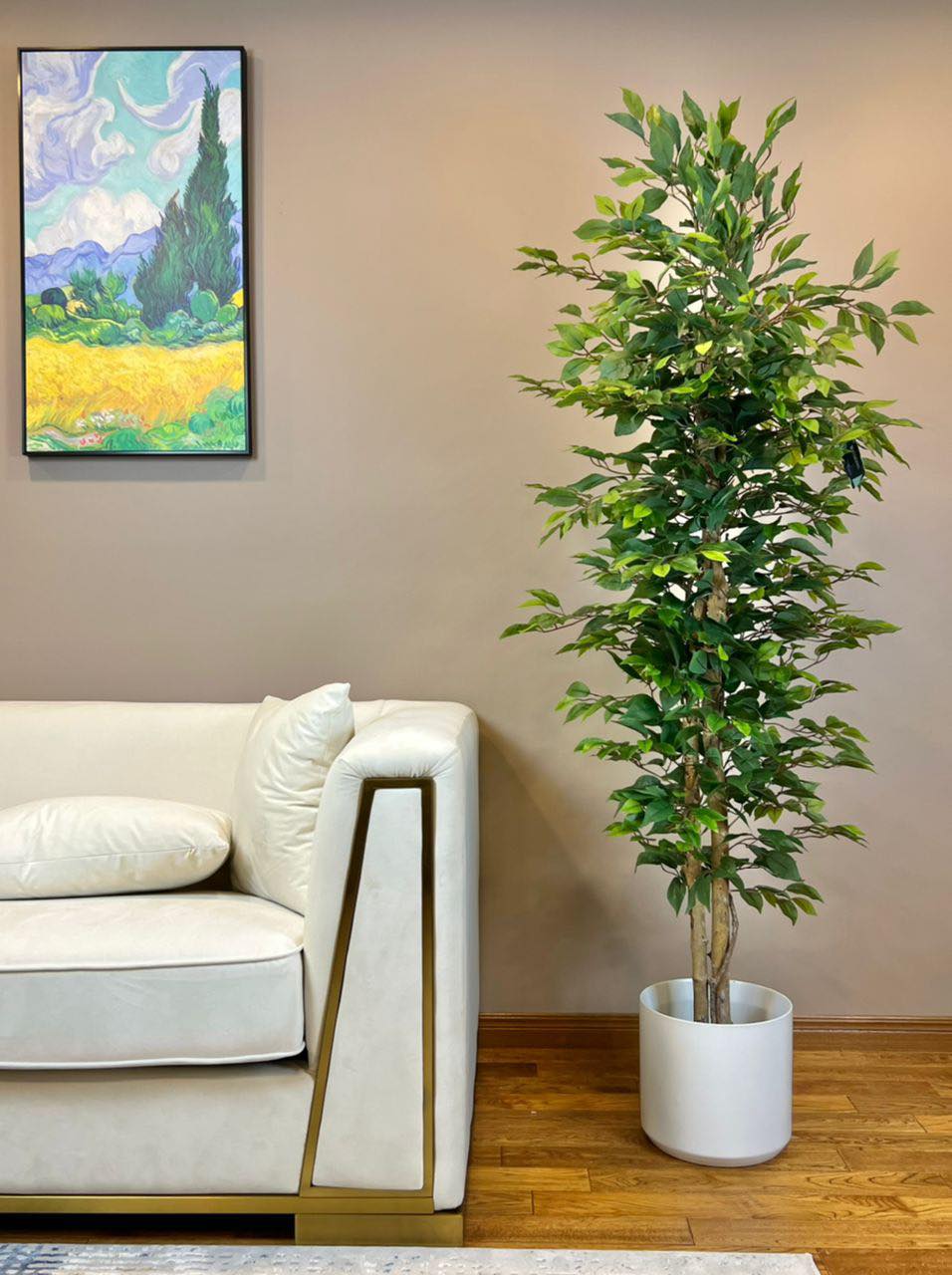 An elegant indoor setting featuring a sleek white couch and a vibrant green potted plant, complemented by a colorful landscape painting on the wall.