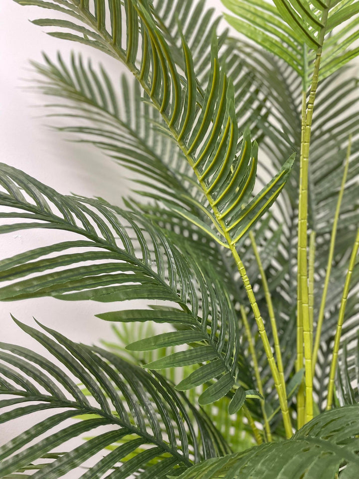 Close-up of a palm tree's artificial trunk, displaying green stems with yellow and brown accents at the base. The detail highlights the textured and realistic design of the tree.
