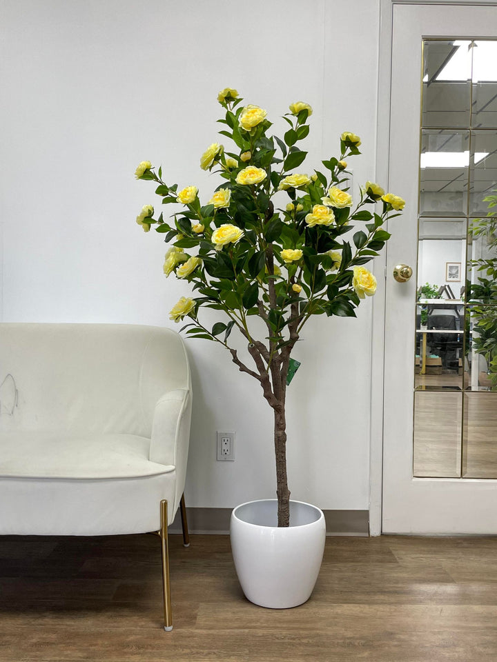 Artificial yellow flower tree in a sleek white pot, positioned beside a modern white chair in a bright and minimalistic room, enhancing the space with a touch of natural beauty.