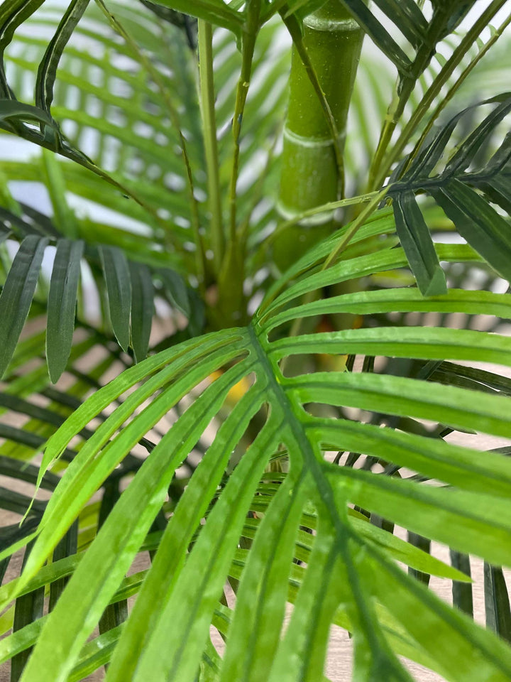 Detailed close-up of artificial palm leaves and bamboo stalk, showcasing realistic textures and vibrant green hues, perfect for home or office décor