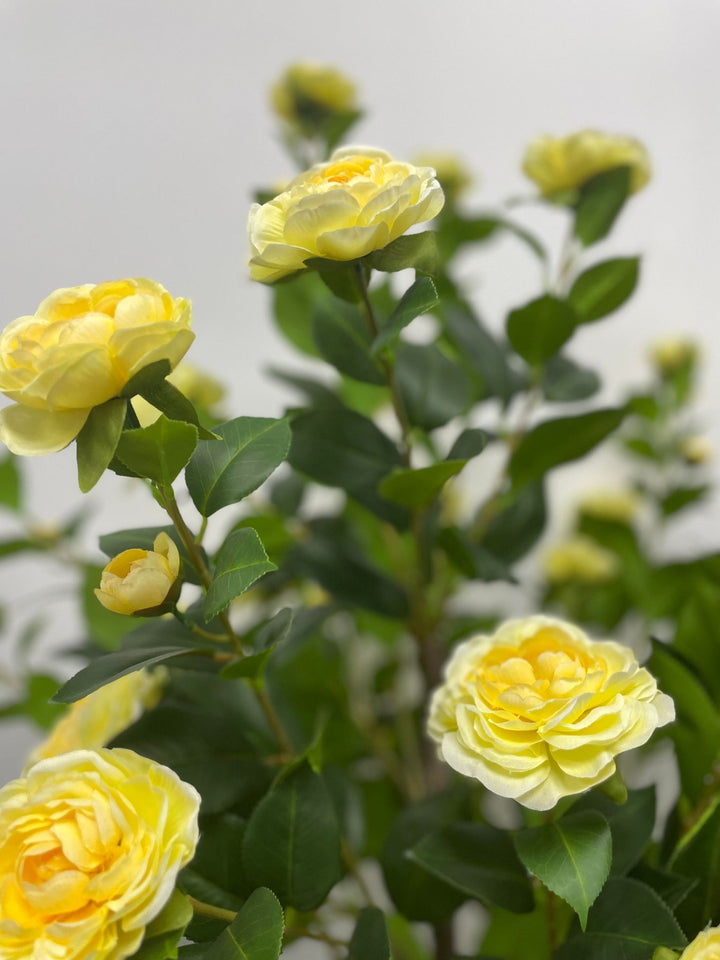 Close-up of artificial yellow flowers with lush green leaves, showcasing intricate details that bring a fresh and vibrant look to any indoor setting.