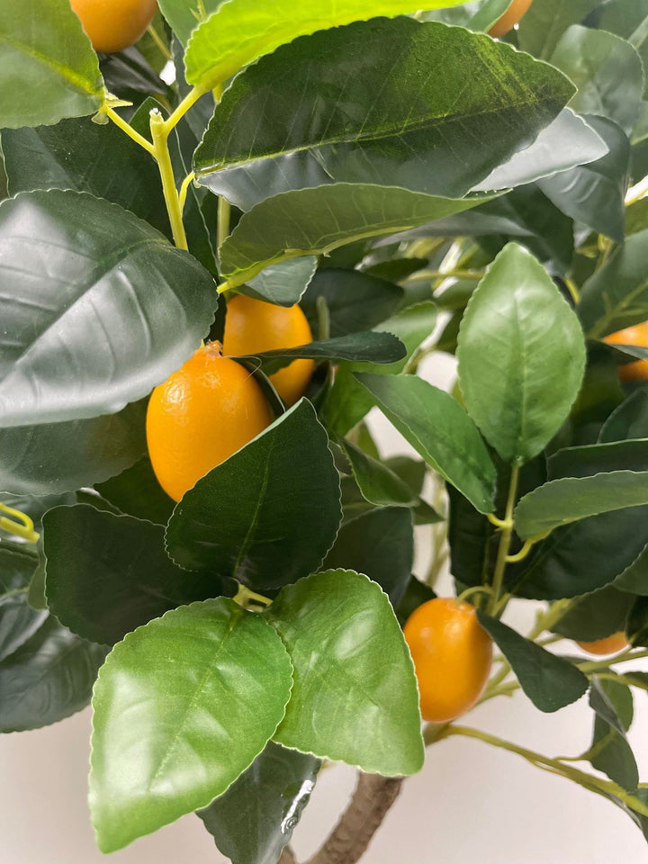 Close-up of an artificial lemon tree with vibrant green leaves and realistic yellow lemons, showcasing lifelike details in a bright indoor environment