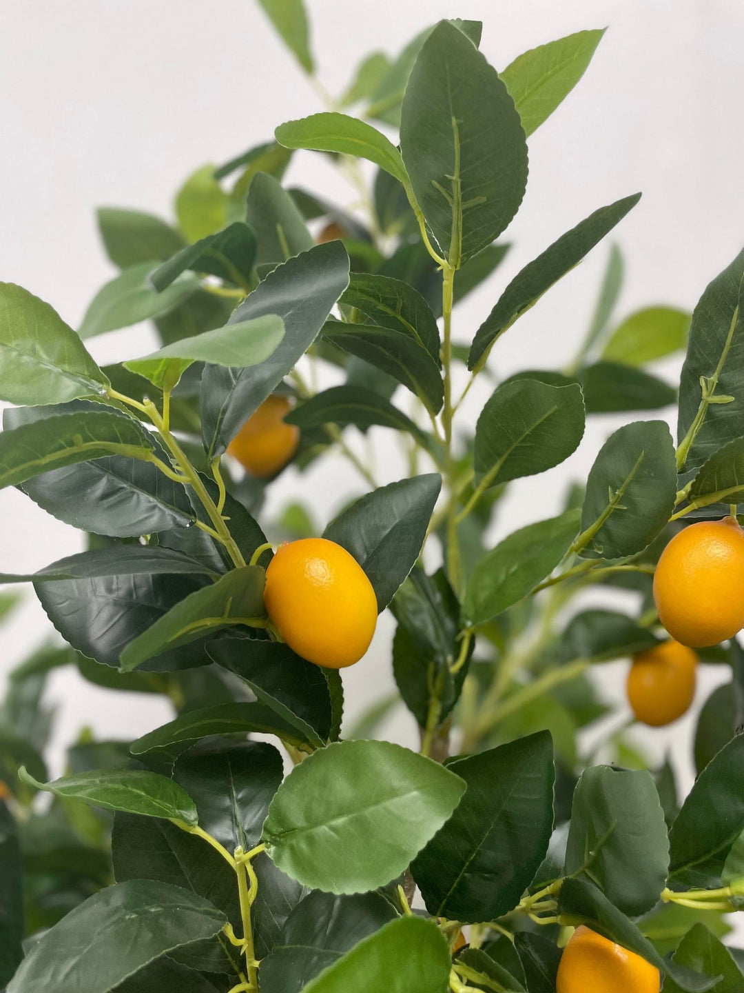Close-up of an artificial lemon tree with vibrant green leaves and realistic yellow lemons, showcasing lifelike details in a bright indoor environment