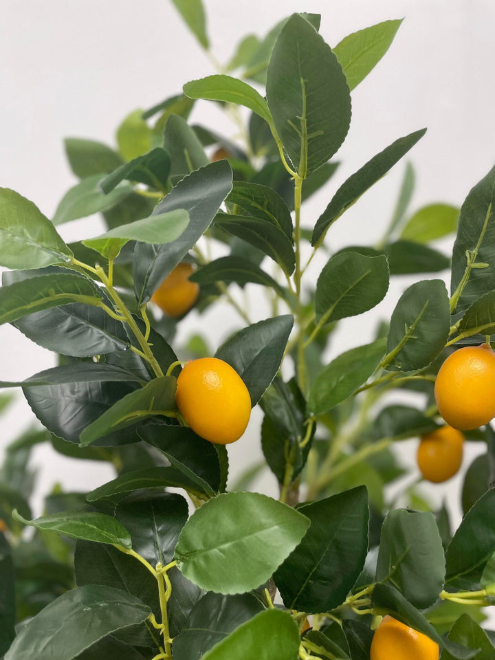 Close-up of an artificial lemon tree with vibrant green leaves and realistic yellow lemons, showcasing lifelike details in a bright indoor environment