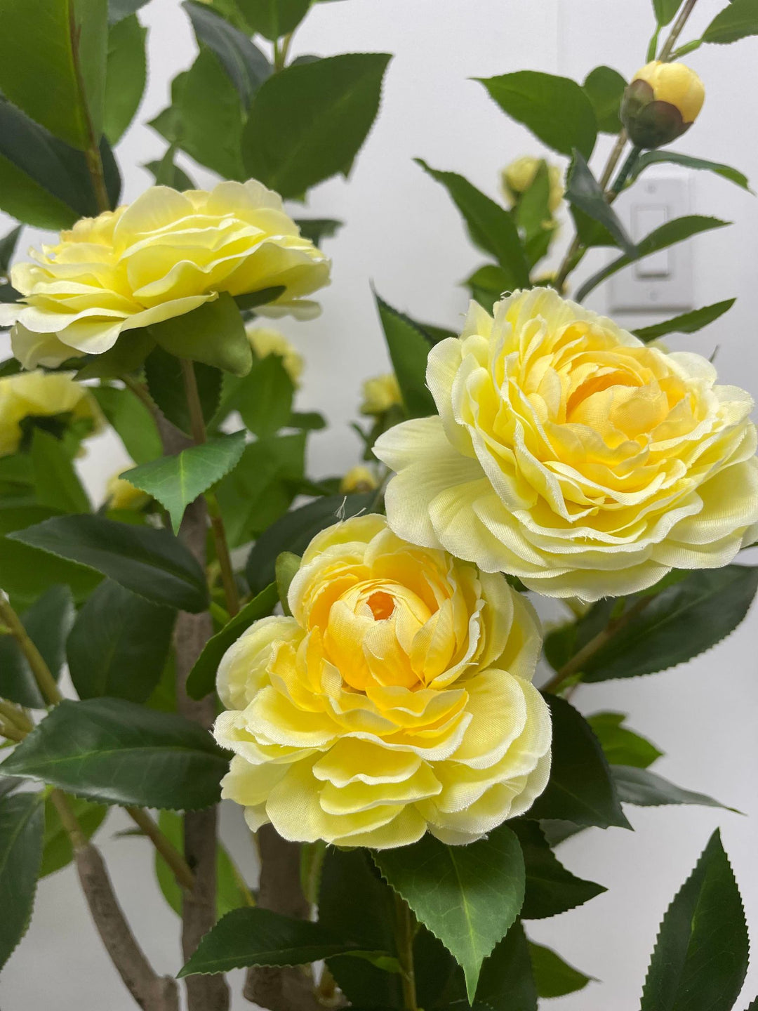 Close-up of artificial yellow flowers with lush green leaves, showcasing intricate details that bring a fresh and vibrant look to any indoor setting.