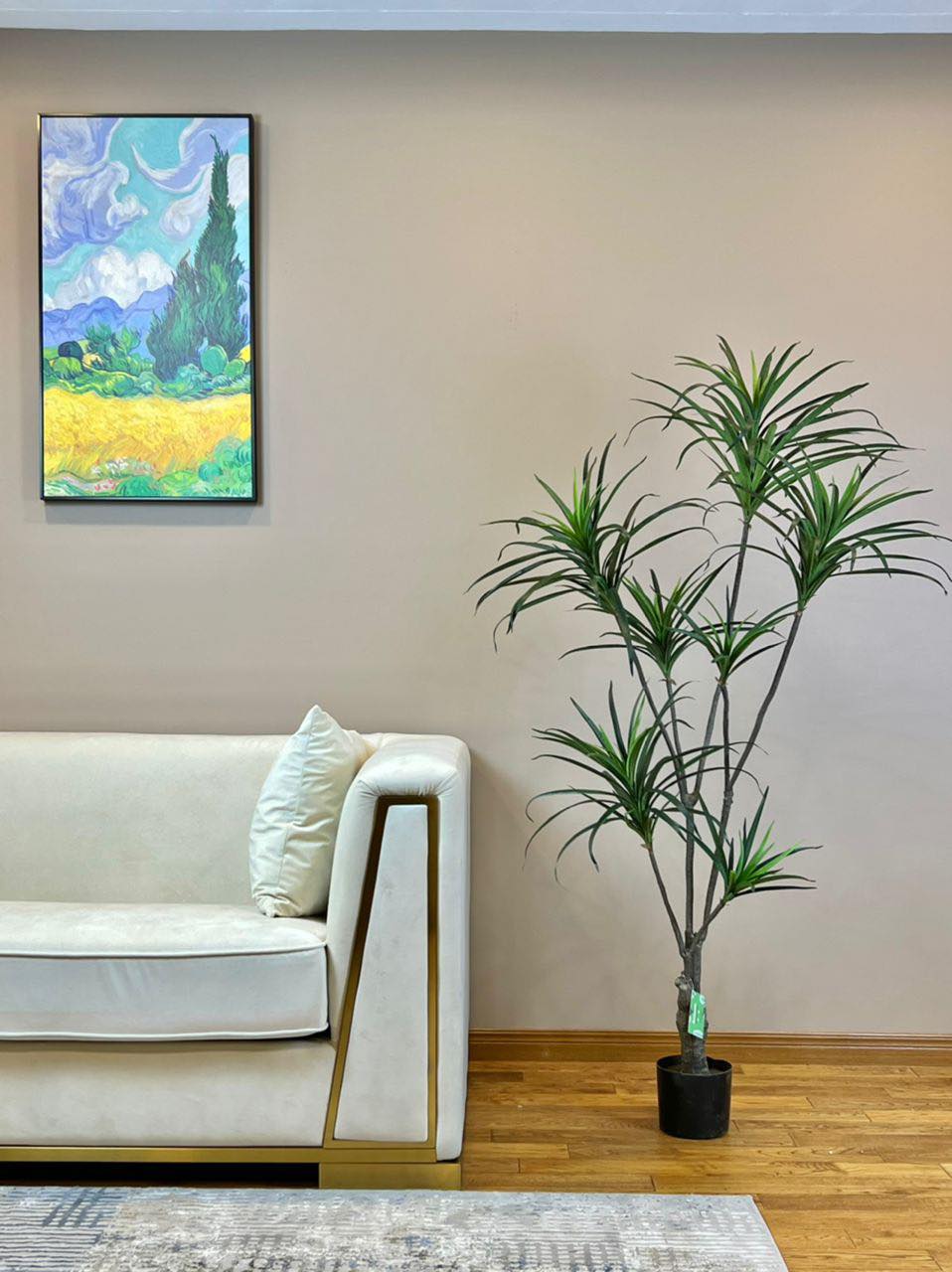 Artificial yucca plant in a modern black planter placed beside a luxurious white sofa with gold accents, enhancing the contemporary decor of a living room with wooden flooring and wall art