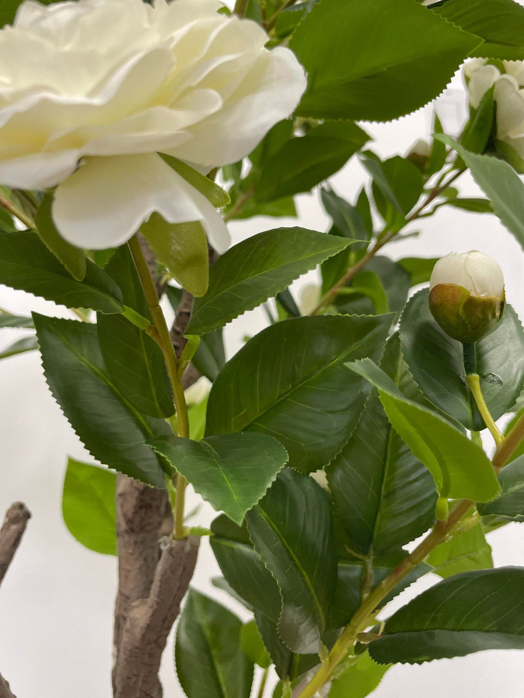 Close-up of an artificial white flower with green leaves and a budding bloom, showcasing intricate details perfect for home or office decor.