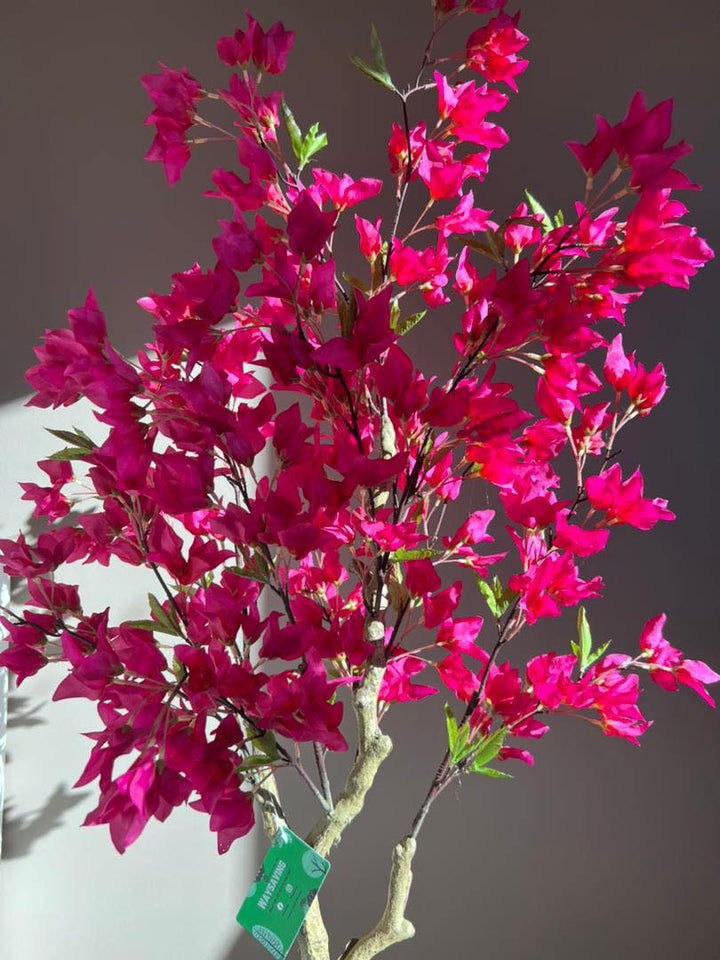 Close-up of an artificial pink flowering tree, with vibrant pink blossoms and green leaves, illuminated by natural sunlight in an indoor setting