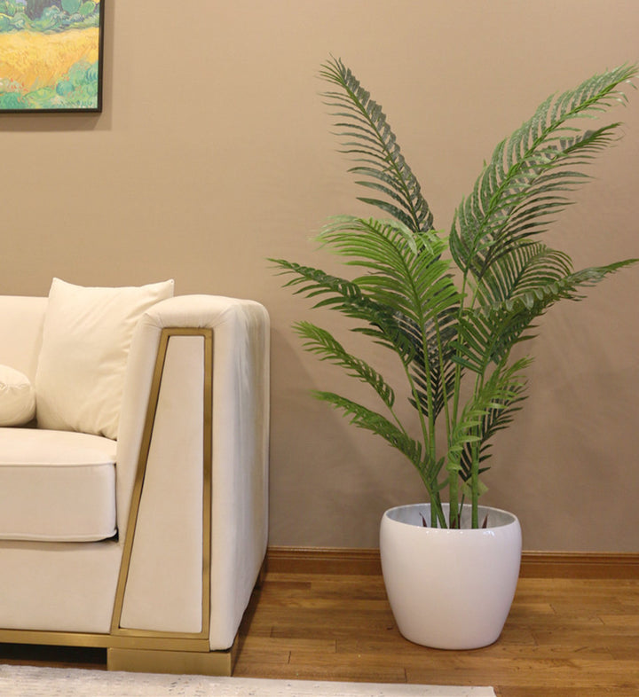 artificial palm tree. Artificial palm tree in a white planter, positioned beside a modern beige couch in a cozy living room.