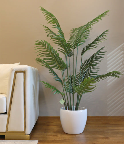 Artificial palm tree with realistic leaves in a white planter beside a modern sofa.