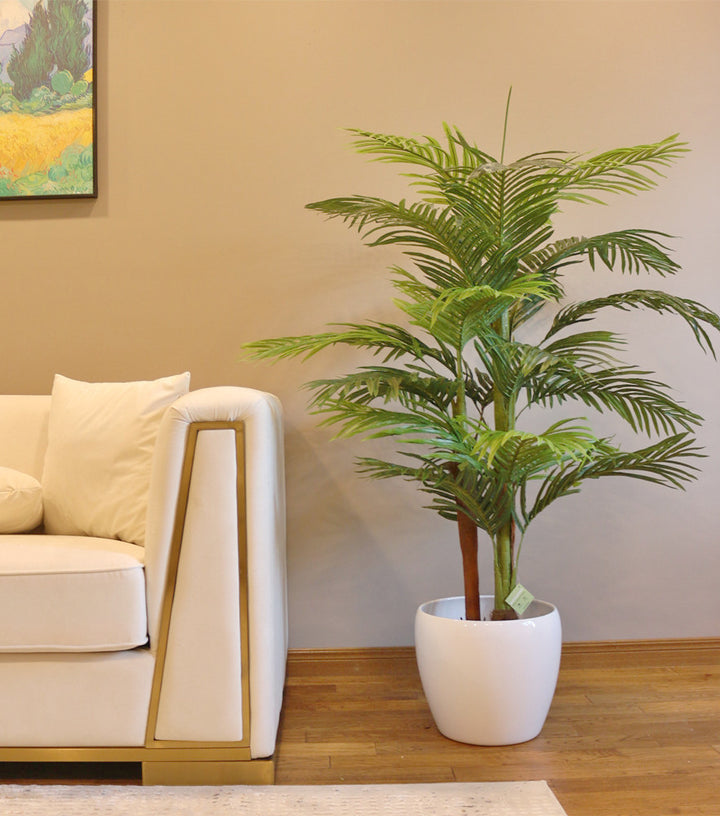 Artificial palm tree- 5.5 ft placed next to a cream armchair in a well-lit corner of a living room.