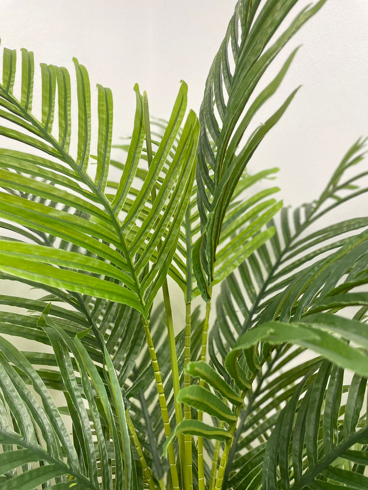 Artificial palm plant in a woven basket, placed on a wooden floor beside a white sofa, enhancing the natural and cozy interior space.