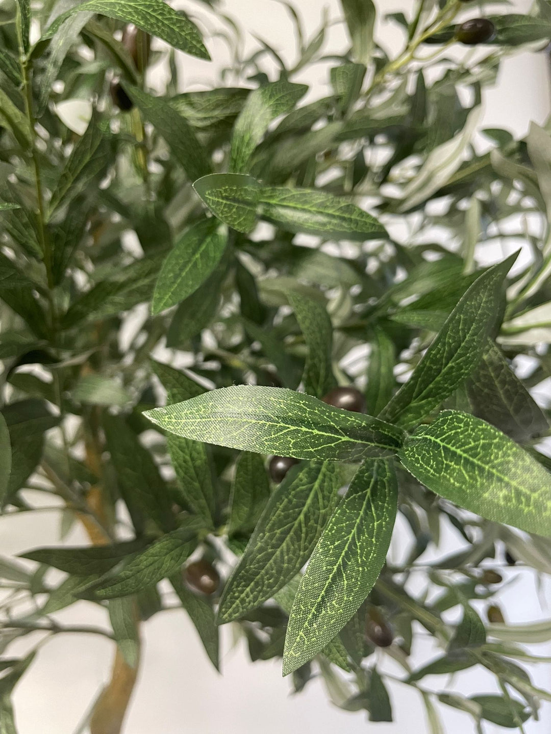 Close-up of artificial olive tree leaves, showcasing the detailed veining and texture of the green foliage, with a few black olives visible in the background