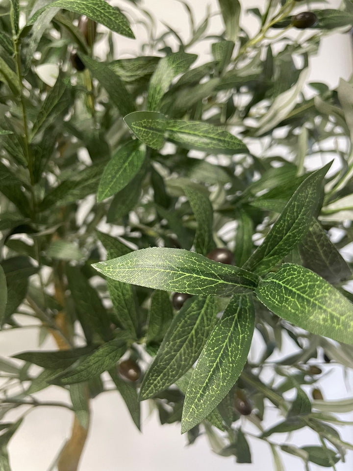 Close-up of artificial olive tree leaves, showcasing the detailed veining and texture of the green foliage, with a few black olives visible in the background
