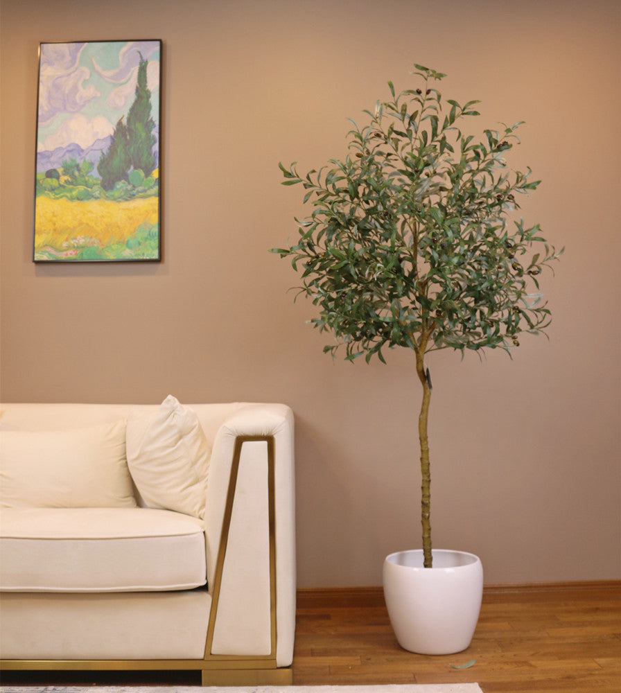 Artificial olive tree with slender green leaves and small black olives in a textured white pot placed near a glass-paneled door in a bright indoor space with wooden flooring.