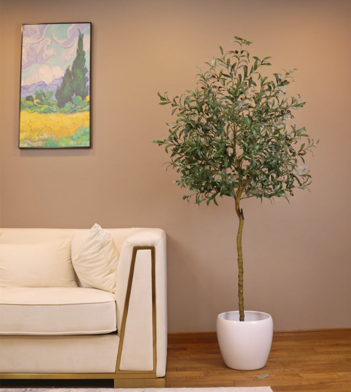 Artificial olive tree with slender green leaves and small black olives in a textured white pot placed near a glass-paneled door in a bright indoor space with wooden flooring.