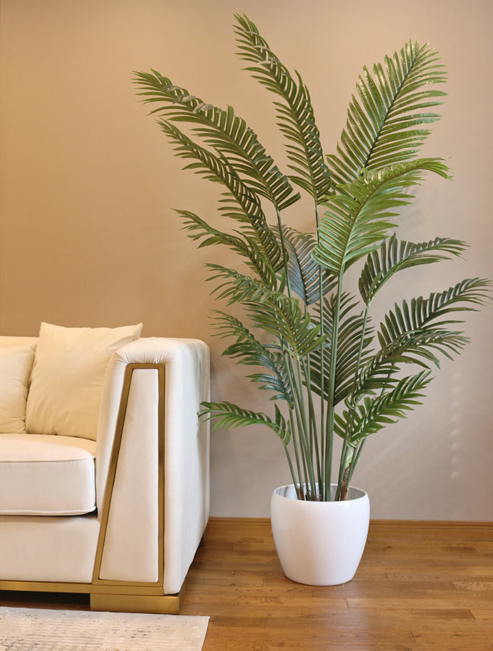 Artificial palm plant in a modern white ceramic pot, placed beside a luxurious white sofa with gold accents, creating a chic and contemporary living room decor