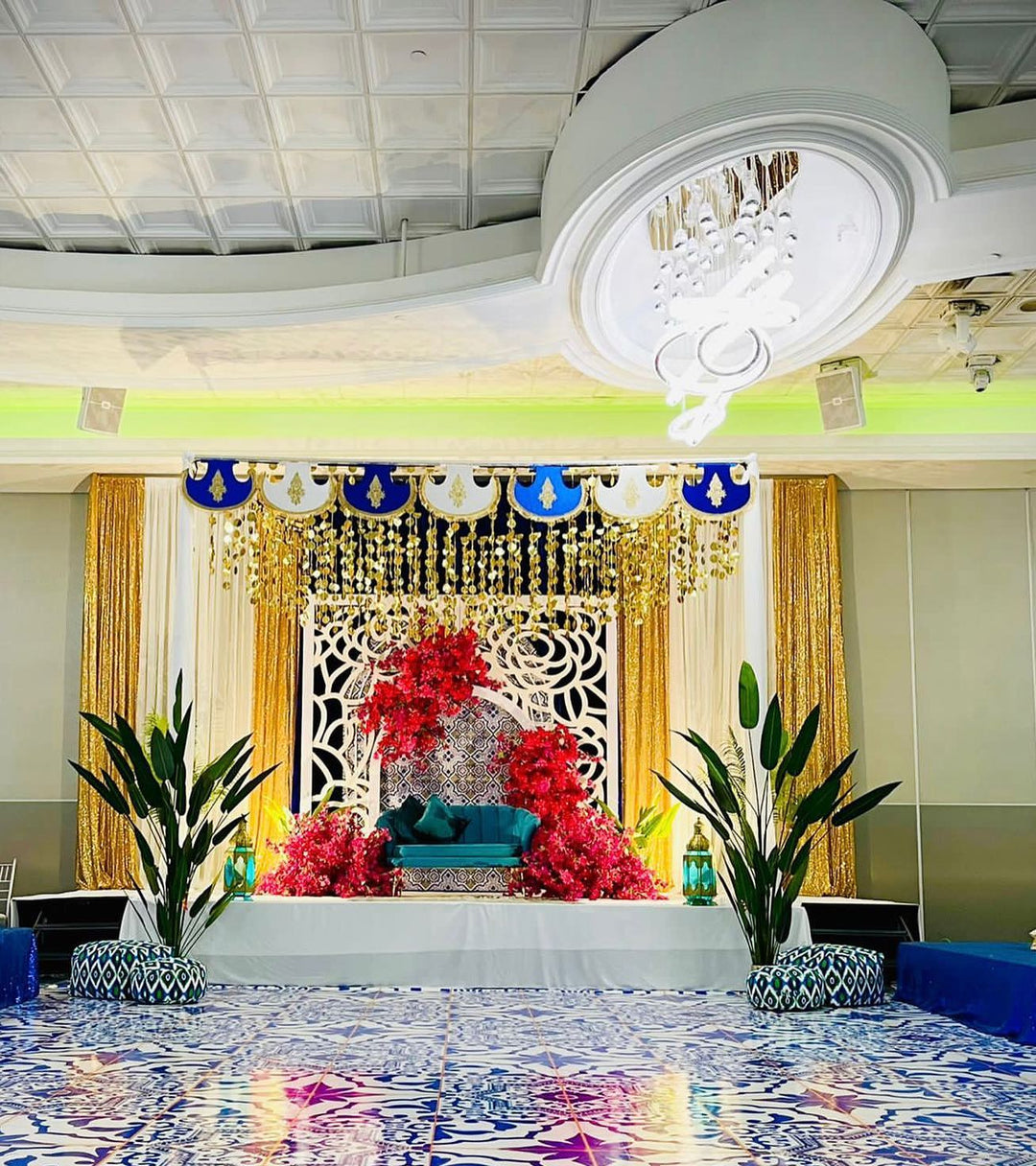 A luxurious event stage decorated with a vibrant setup, featuring 7ft artificial bird of paradise plants and framed by intricate white lattice panels. 