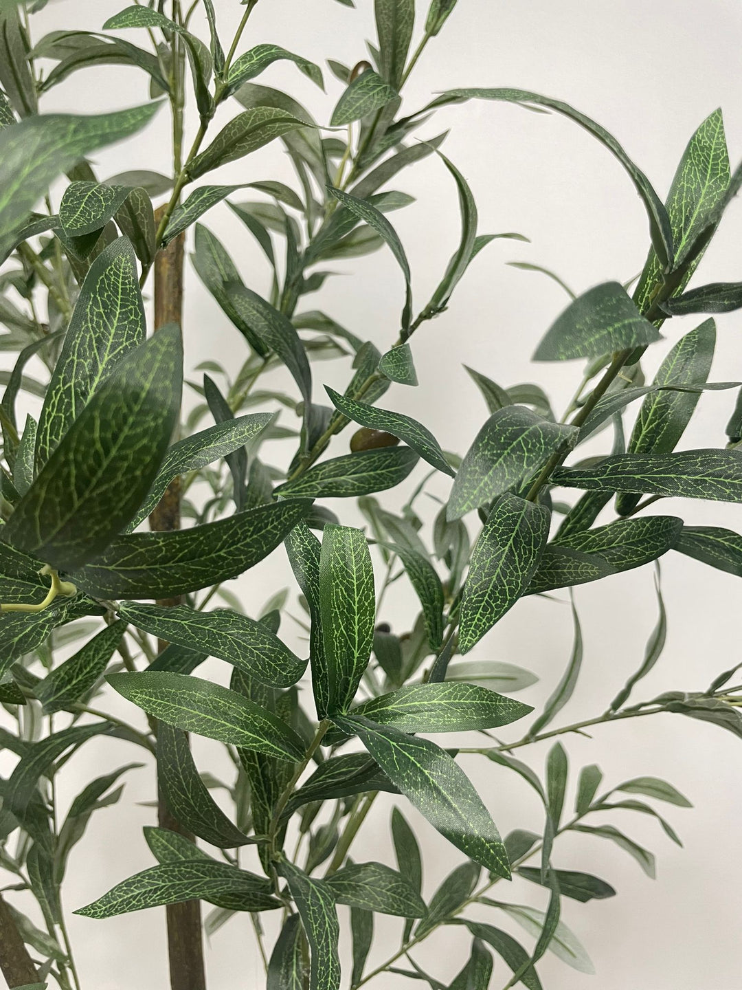 Close-up view of the artificial olive tree's leaves and small dark olives, showing the detailed texture and realistic design of the foliage against a neutral background.