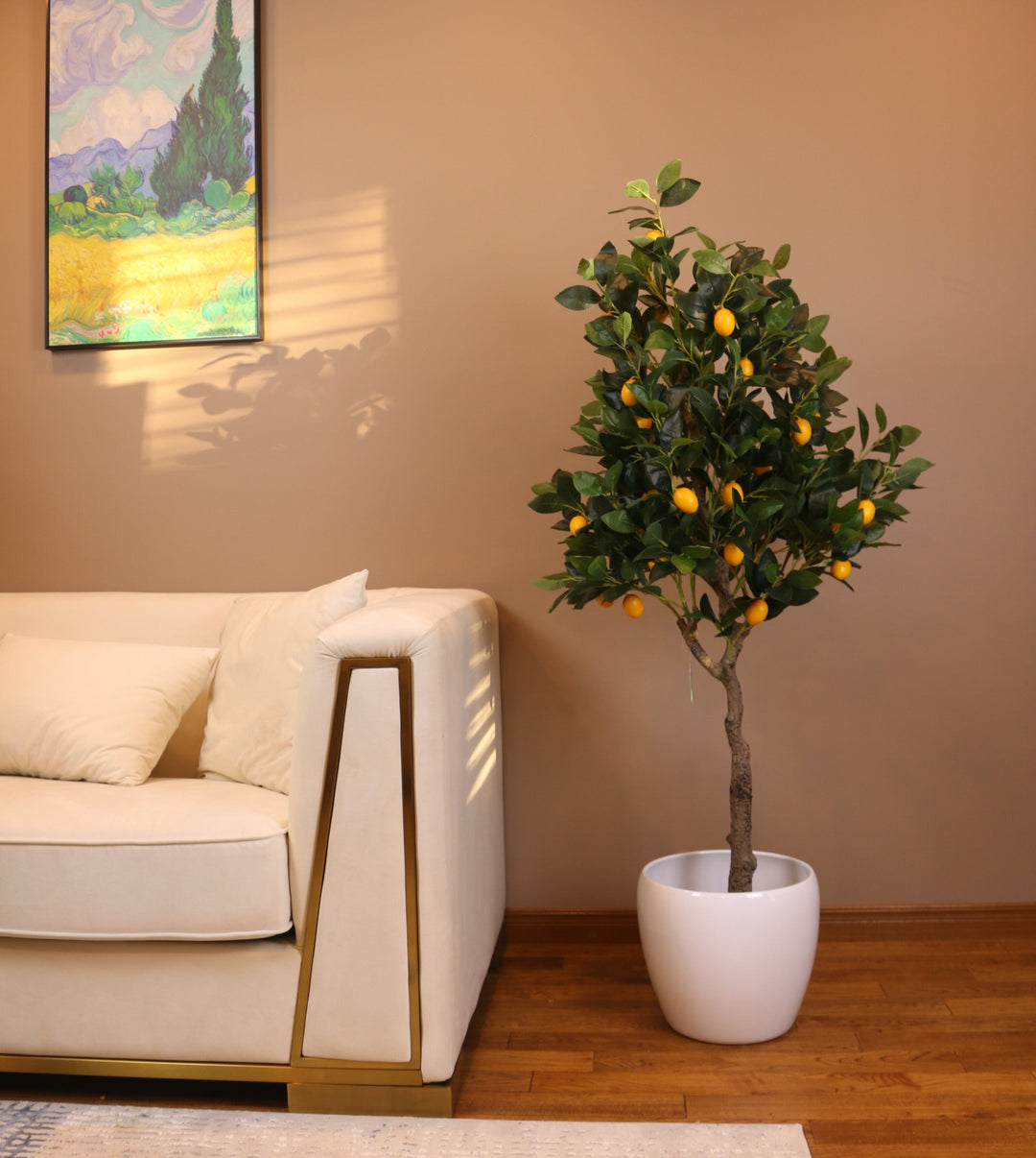 Artificial lemon tree with realistic green leaves and vibrant yellow lemons, placed in a black planter beside a white armchair, perfect for adding a touch of nature to indoor spaces.