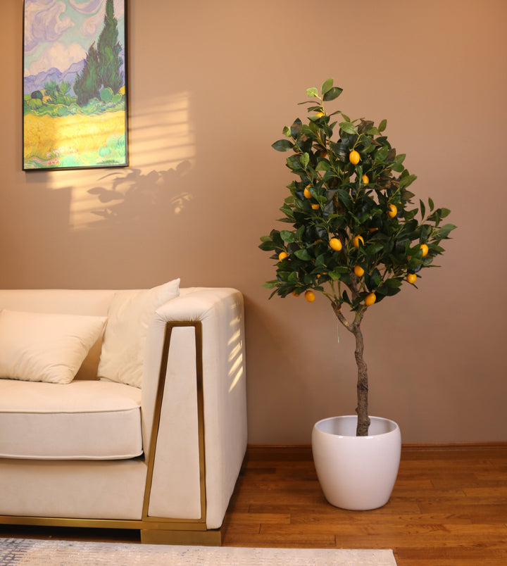 Artificial lemon tree with realistic green leaves and vibrant yellow lemons, placed in a black planter beside a white armchair, perfect for adding a touch of nature to indoor spaces.