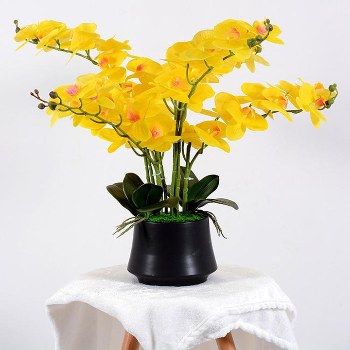 Elegant arrangement of artificial yellow orchids in a sleek black pot. The vibrant yellow flowers cascade gracefully, complemented by lush green leaves, making it a perfect decorative piece for adding a pop of color to any space