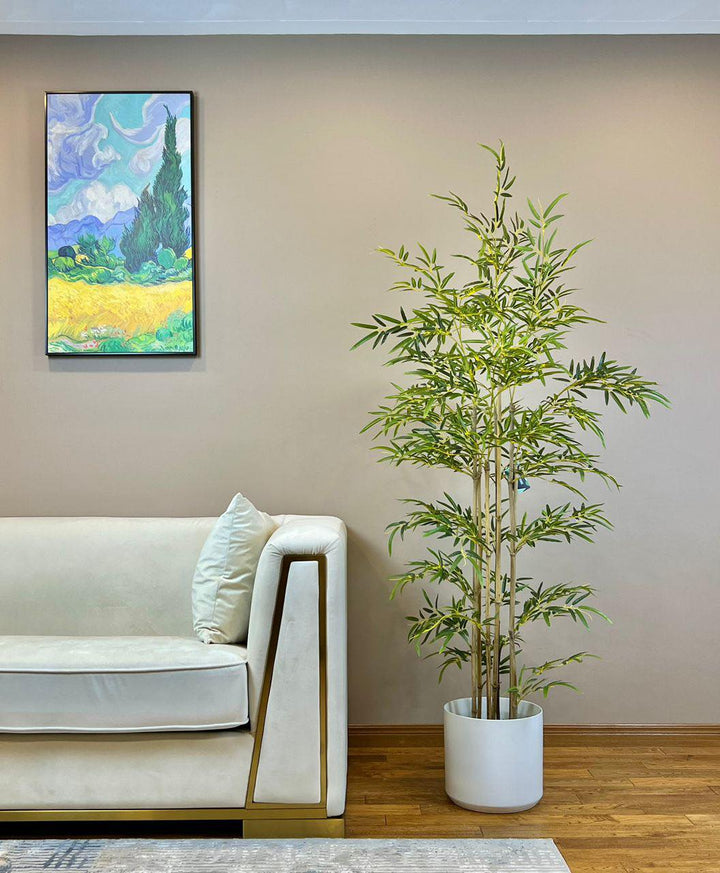 Elegant artificial bamboo plant in a white pot, placed next to a modern white sofa in a stylish living room.