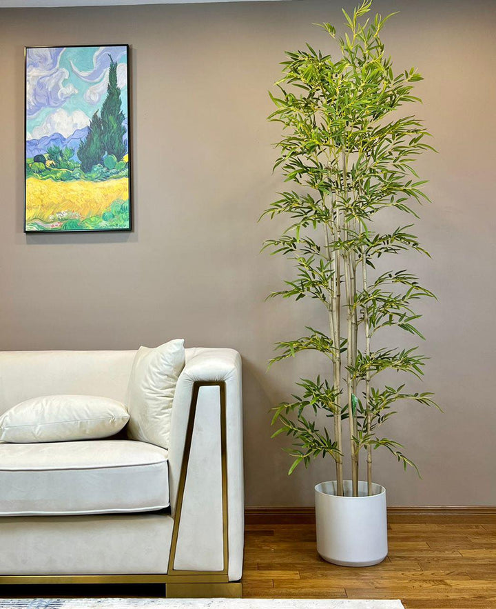 Modern living room with a tall, lifelike artificial bamboo plant in a sleek white pot, positioned beside a white sofa.