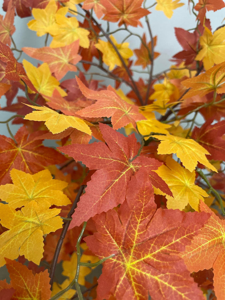 Close-up of vibrant artificial autumn maple leaves in shades of red, orange, and yellow, showcasing detailed veins and texture.