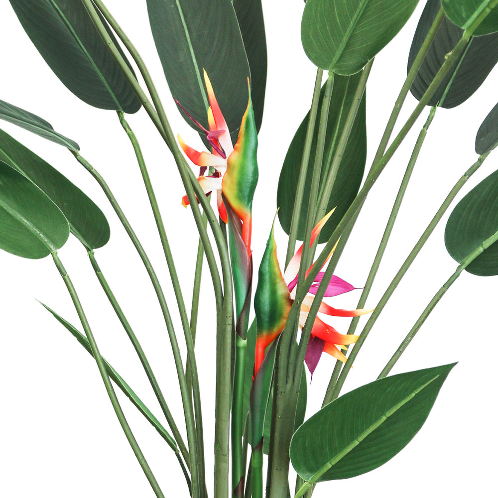 Close-up view of an artificial Bird of Paradise plant showing the vibrant orange and yellow flowers nestled among tall green stems and large, glossy green leaves