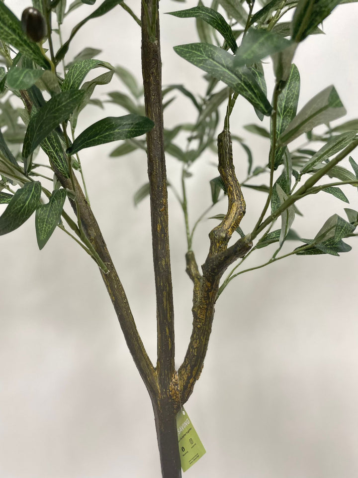 Close-up of the detailed trunk and branches of an artificial olive tree with a textured, lifelike appearance. A green tag with the brand name "Waysaving" is attached to one of the branches. The tree features realistic bark textures and connected branches, making it a convincing decorative piece for indoor settings.