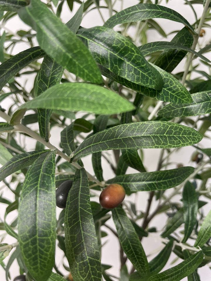 Close-up view of the artificial olive tree's leaves and small dark olives, showing the detailed texture and realistic design of the foliage against a neutral background
