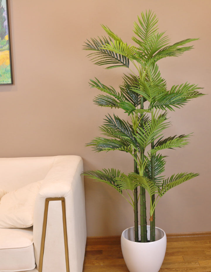 Modern living room featuring a stylish white sofa with gold accents, a vibrant green palm tree in a white planter, and a colorful framed artwork on the wall.