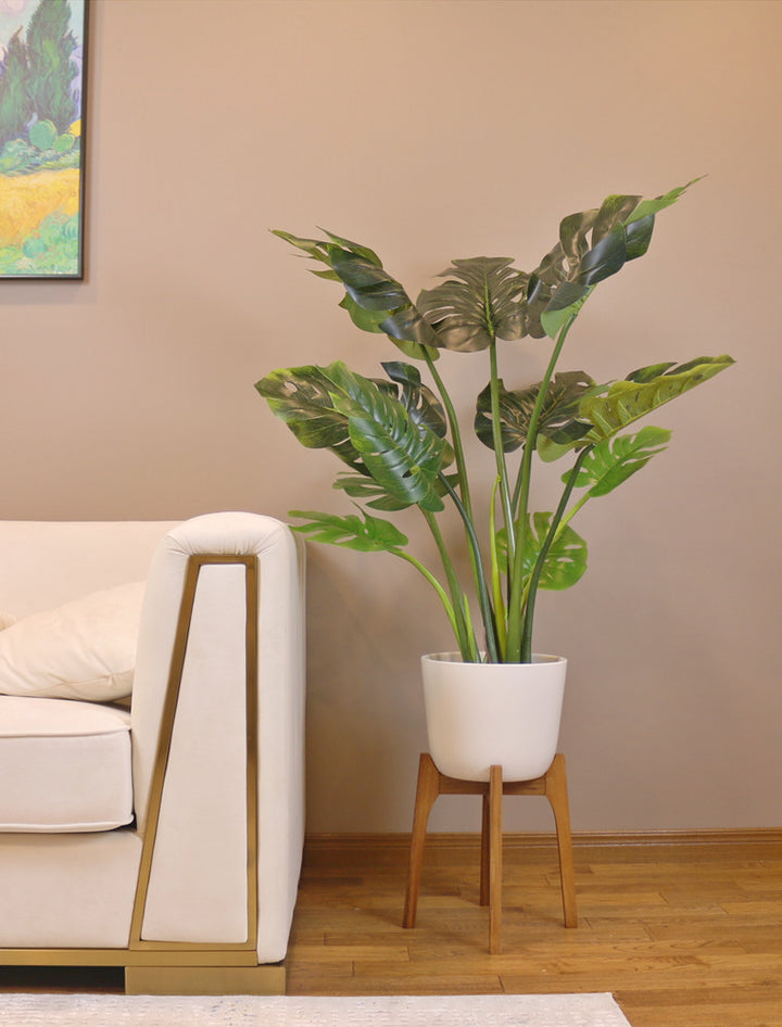 Large artificial monstera plant with vibrant green, split leaves, displayed in a sleek white pot on a wooden floor, enhancing the indoor decor with a tropical touch.